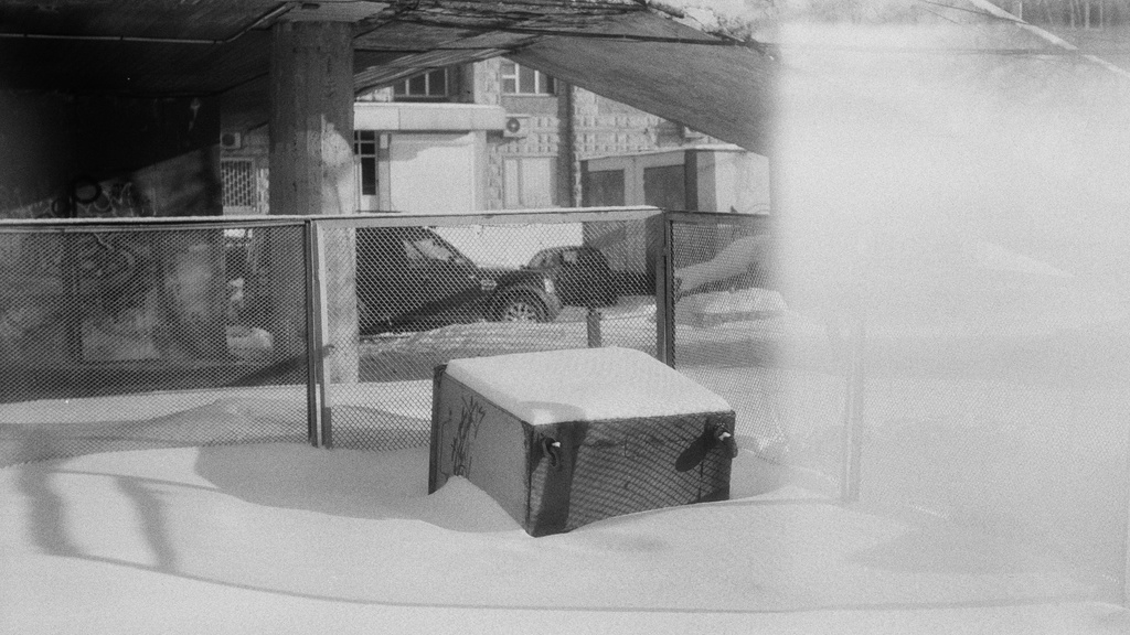 Black and white photo of a snowy yard surrounded by a fence.